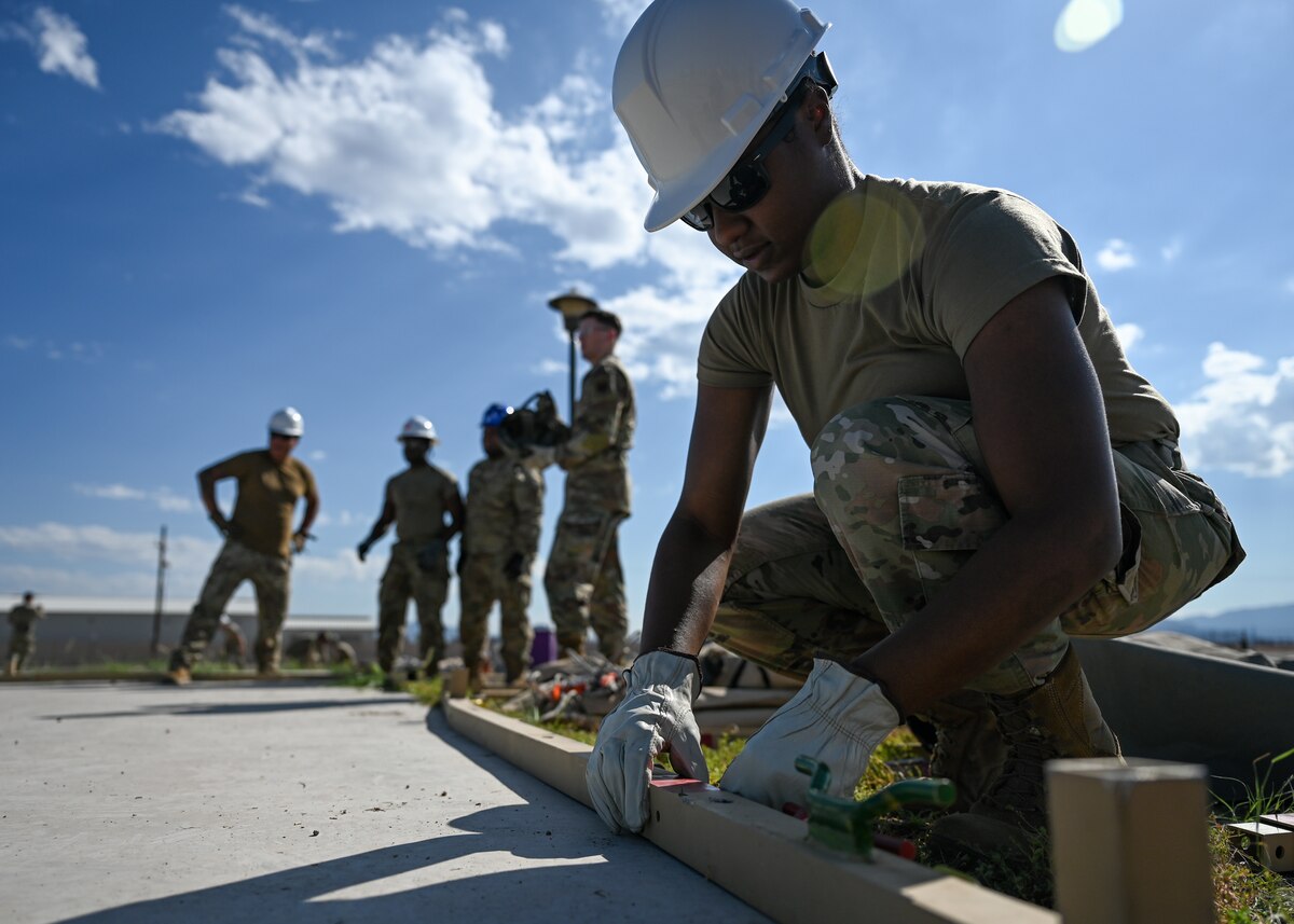 A photo of a person in a military uniform assembling the metal structure of a large tent.