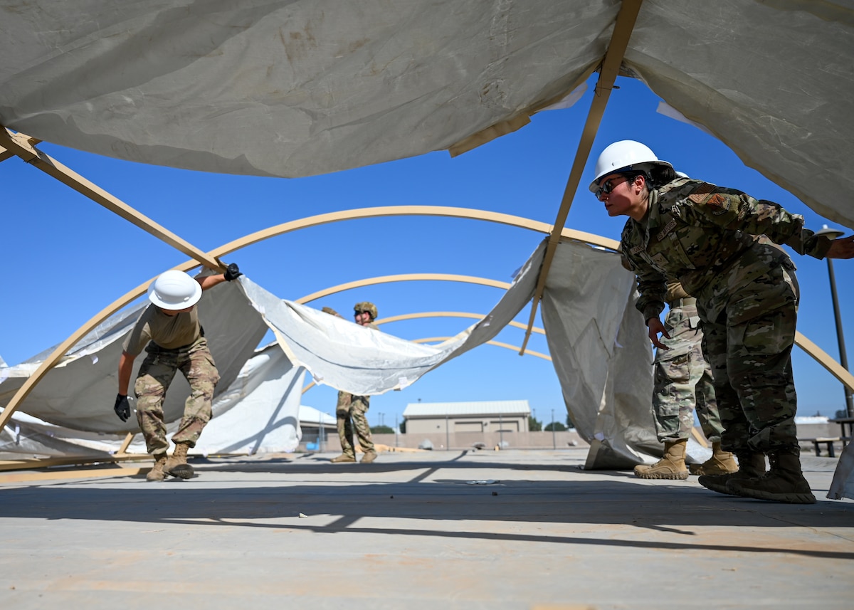 A photo of people in military uniforms assembling a large tent.