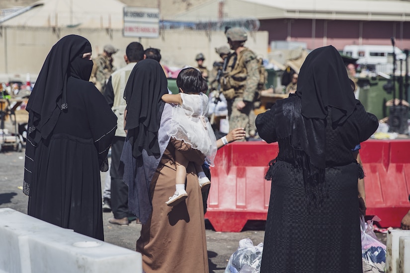 Military personnel assist people standing in a line.