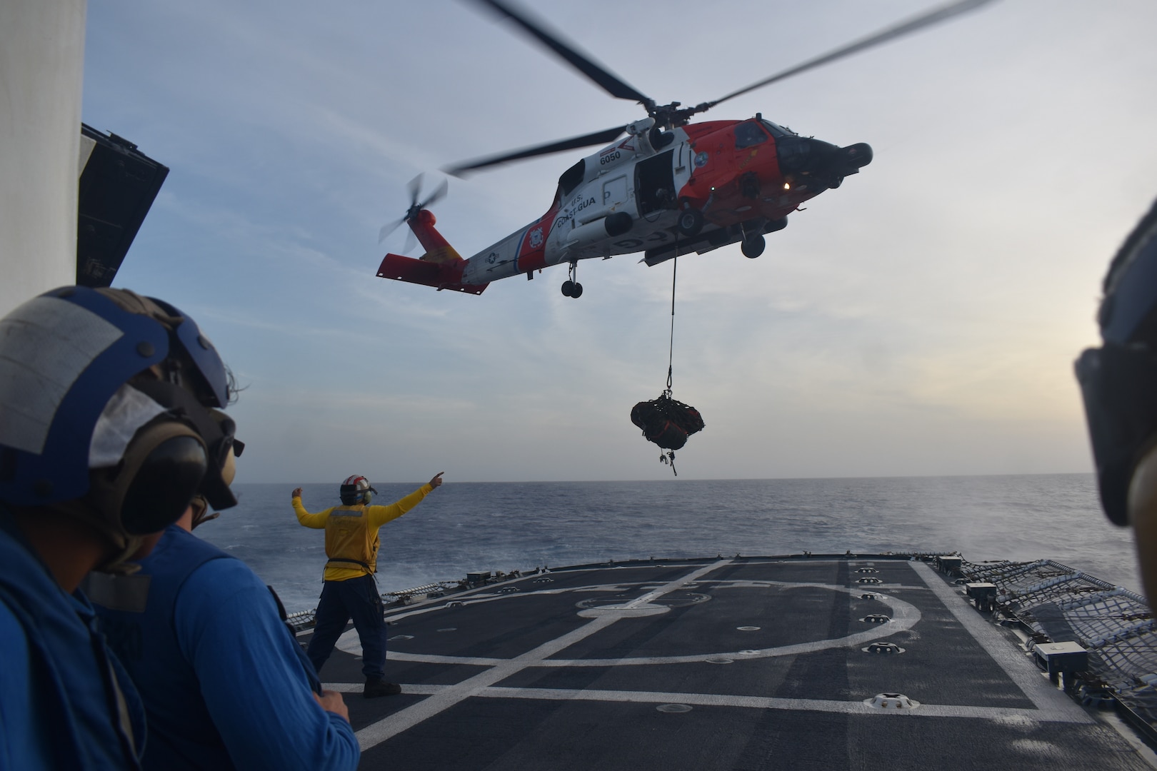 U.S. Coast Guard Ensign Chase Sanders, a landing signal officer assigned to Coast Guard Cutter Resolute (WMEC 620), directs a Coast Guard Jayhawk MH-60 helicopter to hover off Resolute’s port side during a vertical replenishment exercise in the Caribbean Sea, July 27, 2023. A Coast Guard aircraft crew out of Great Inagua, Bahamas, conducted in-flight refueling, vertical replenishment, and rescue basket training during Resolute’s patrol supporting Operation Vigilant Sentry. (U.S. Coast Guard photo courtesy of Resolute)