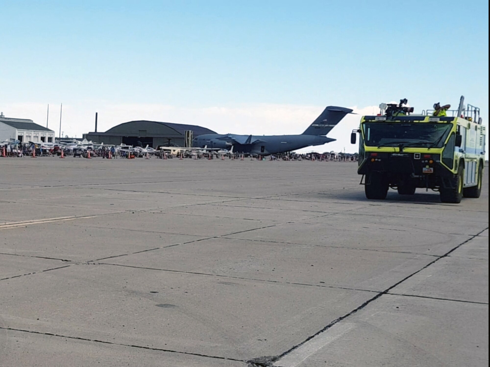 A fire truck sits on the flight line with a C-17 in the background