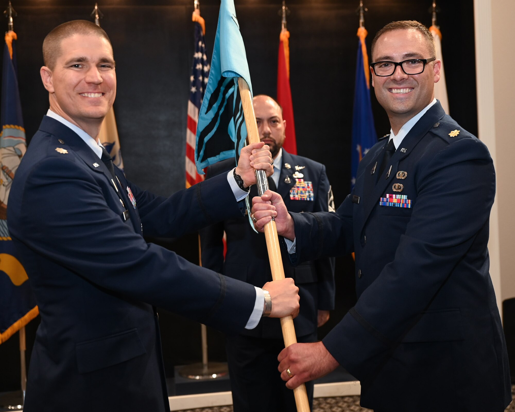U.S. Space Force Lt. Col. Jonathan R. Arehart, 533rd Training Squadron commander, left, passes the 533rd TRS, Detachment 1 guidon to Maj. Benjamin Tillman, right, incoming commander, during the 533rd TRS, Detachment 1 Change of Command Ceremony at the Powell Event Center, Goodfellow Air Force Base, Texas, Aug. 29, 2023. This was the first-ever Change of Command Ceremony held for the detachment. (U.S. Air Force photo by Airman 1st Class Evelyn J. D’Errico)