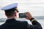 Lt. j. g. David Moya, a chaplain assigned to the Arleigh Burke-class guided-missile destroyer USS Paul Ignatius (DDG 117) takes a photo from the pier at Naval Station (NAVSTA) Rota as the ship returns from deployment, Nov. 28, 2023. As the "Gateway to the Mediterranean,” NAVSTA Rota provides U.S, NATO and allied forces a strategic hub for operations in Europe, Africa and the Middle East. NAVSTA Rota is a force multiplier, capable of promptly deploying and supporting combat-ready forces through land, air and sea, enabling warfighters and their families, sustaining the fleet and fostering the U.S. and Spanish partnership. (U.S. Navy photo by Mass Communication Specialist 2nd Class Drace Wilson)