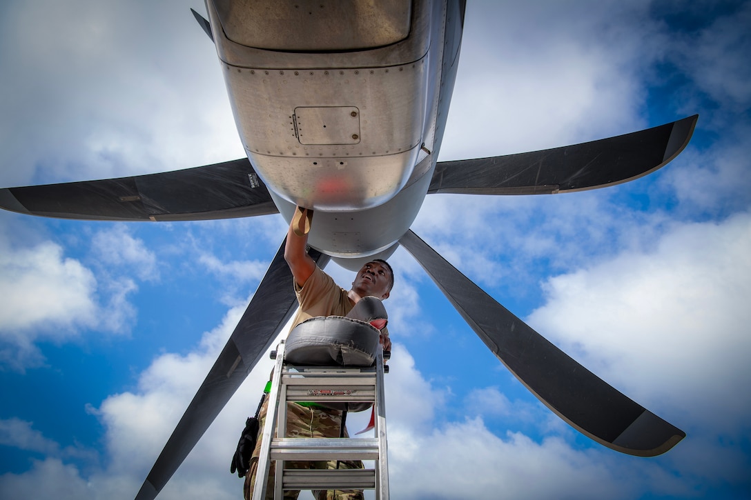 An airman inspects the area behind a propeller on a plane.