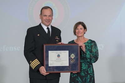 CAPT Anderson stands with Jean Cox holding a plaque