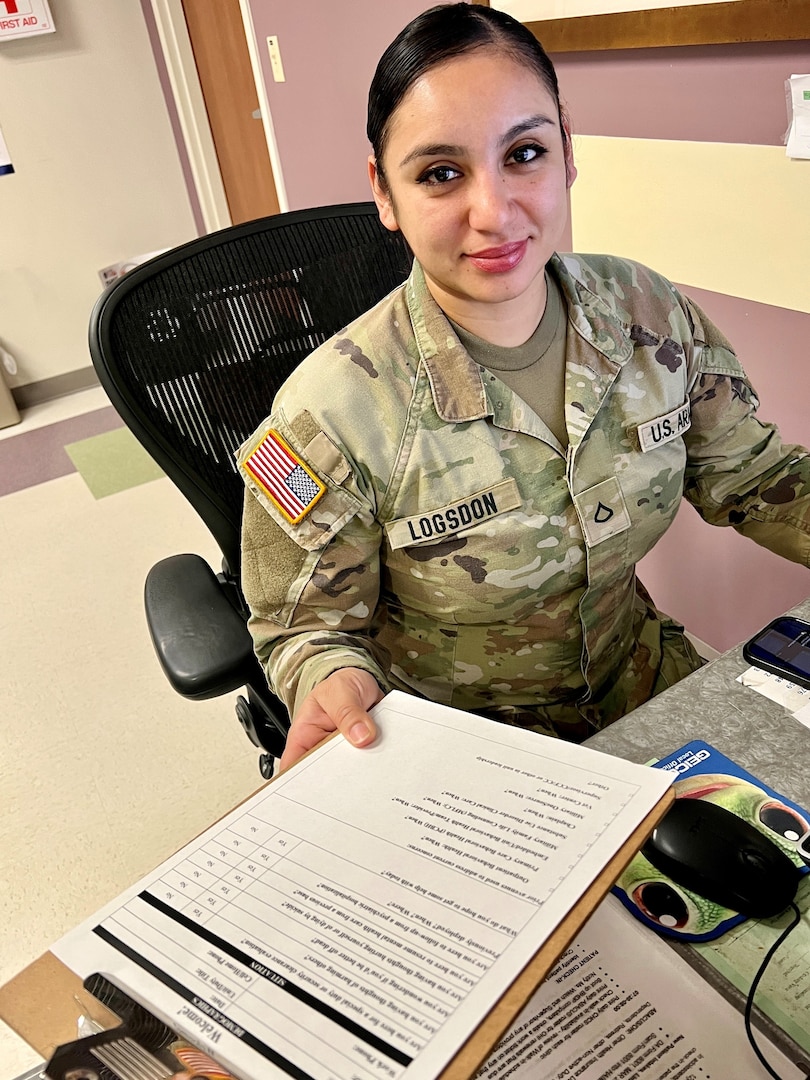 Female Soldier sitting at desk holding an open folder.