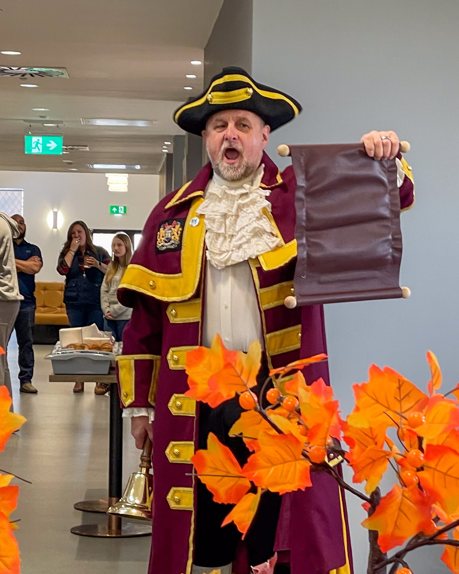 A traditional British town crier holds an open scroll while making an announcement.