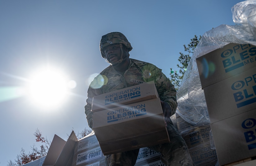 U.S. Army Cpl. George Sanders, 11th Transportation Brigade (Expeditionary) Oshkosh Heavy Expanded Mobility Tactical Truck operator, unloads food kits from the raised pallets during a Thanksgiving turkey give-away at Joint Base Langley-Eustis, Virginia, Nov. 16, 2023.