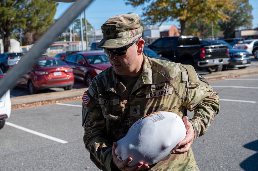 U.S. Army Staff Sgt. Jason Davis, an aircraft power train repair air instructor, 128th  Aviation Brigade aircraft power train repair air instructor, loads a frozen turkey into a trunk during a Thanksgiving turkey give-away at Joint Base Langley-Eustis, Virginia, Nov. 16, 2023.