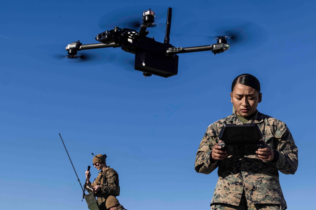 A Marine operates an unmanned aircraft system as another Marine stands behind using equipment.