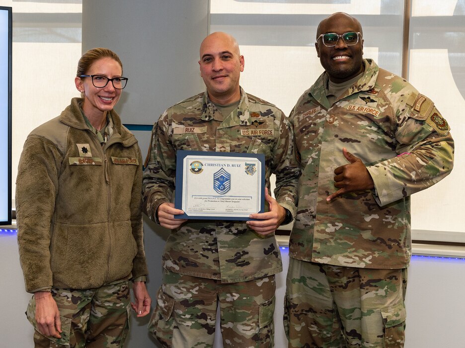 U.S. Air Force Lt. Col. Randon Davis, left, 436th Aerial Port Squadron commander, and U.S. Air Force Chief Master Sgt. William Charles, right, 436th APS senior enlisted leader, present U.S. Air Force Senior Master Sgt. Christian Ruiz, 436th APS air freight superintendent, with a certificate announcing his selection to chief master sergeant at Dover Air Force Base, Delaware, Nov. 29, 2023. Ruiz was one of 506 Airmen selected for promotion to the top enlisted rank of chief for the 23E9 promotion cycle. (U.S. Air Force photo by Roland Balik)
