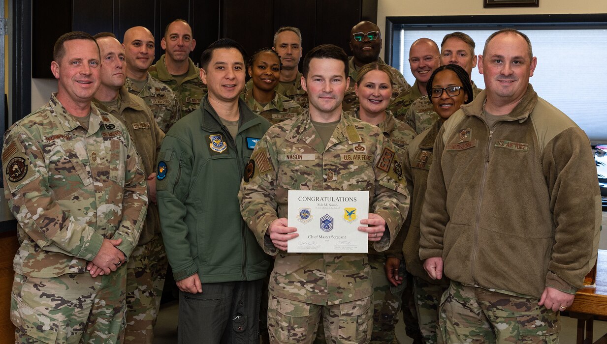 U.S. Air Force Senior Master Sgt. Kyle Nason, 436th Civil Engineer Squadron Explosive Ordnance Disposal flight superintendent, holds his certificate while standing among chief master sergeants, announcing his selection to chief master sergeant at Dover Air Force Base, Delaware, Nov. 29, 2023. Nason was one of 506 Airmen selected for promotion to the top enlisted rank of chief for the 23E9 promotion cycle. (U.S. Air Force photo by Roland Balik)