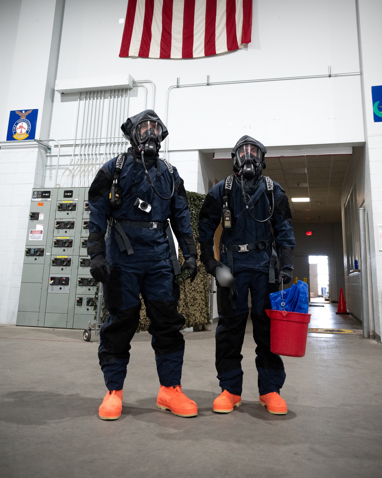 Two people in blue HAZMAT suits stand next to each other.