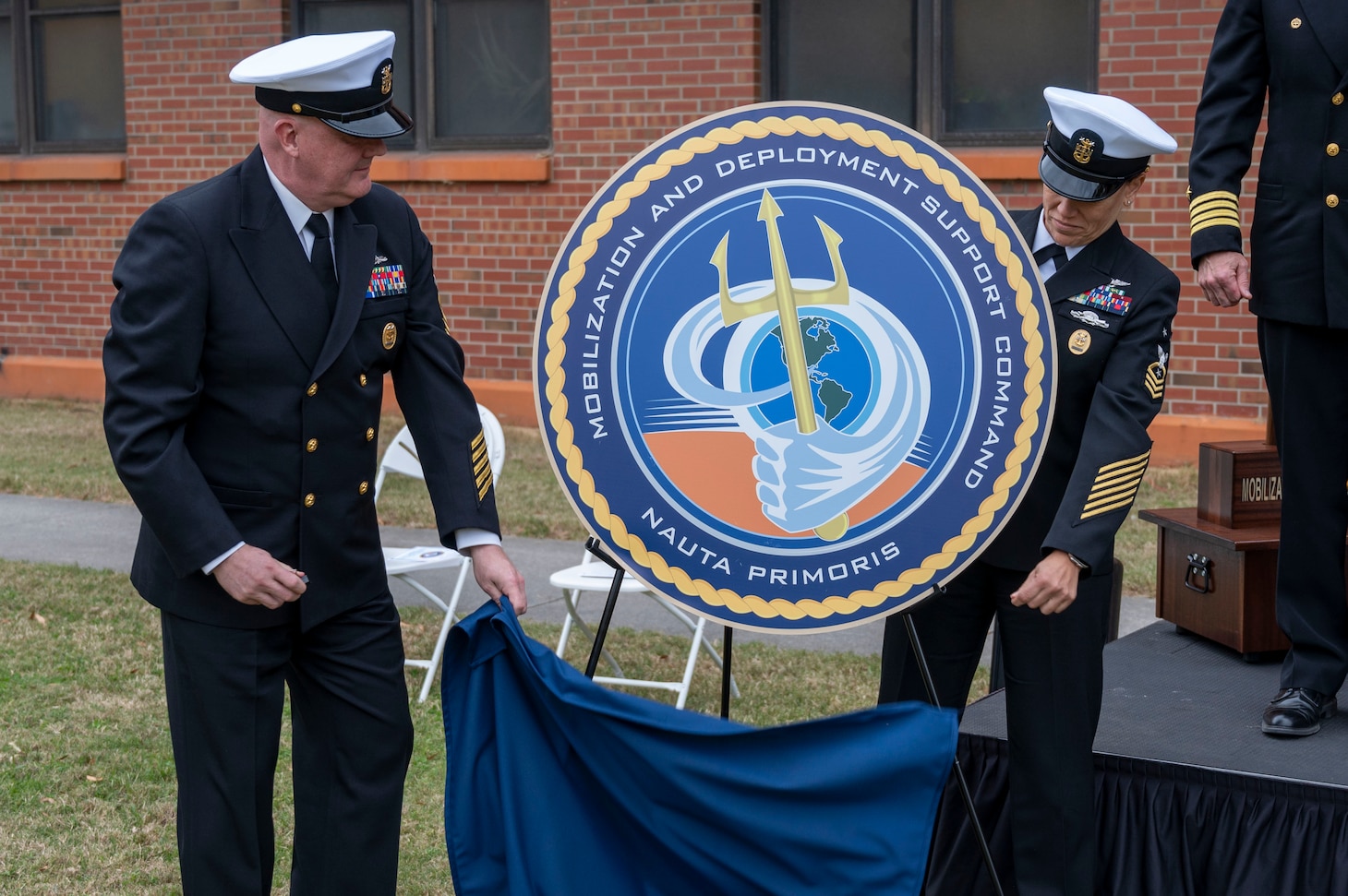 Command Master Chief Nicole Rios and Command Master Chief Michael Harvie unveil the seal for Mobilization and Deployment Support Command during the launch ceremony for Mobilization and Deployment Support Command.
