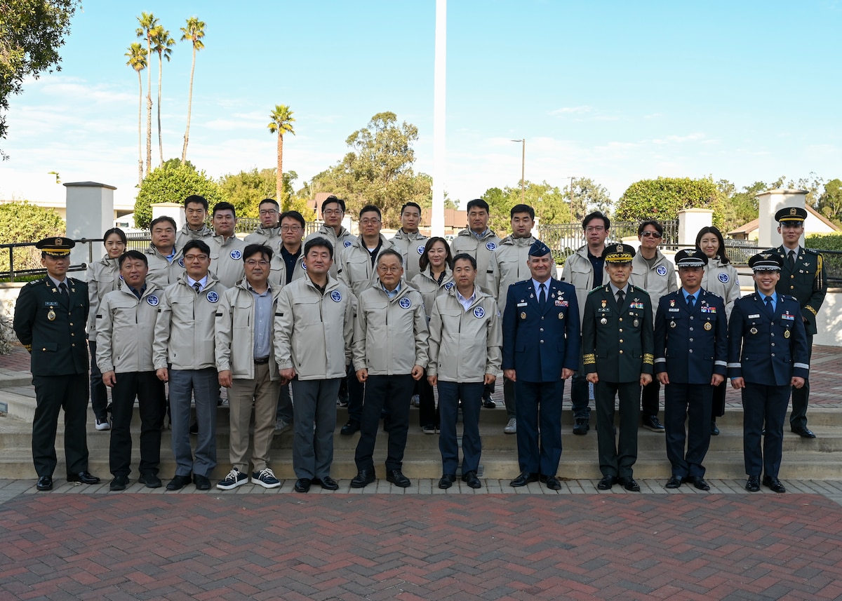 The Republic of Korea team stands in front of a flag pole outside with Colonel Shoemaker.