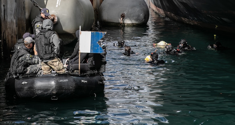 Divers swim in the ocean near the hull of a ship.