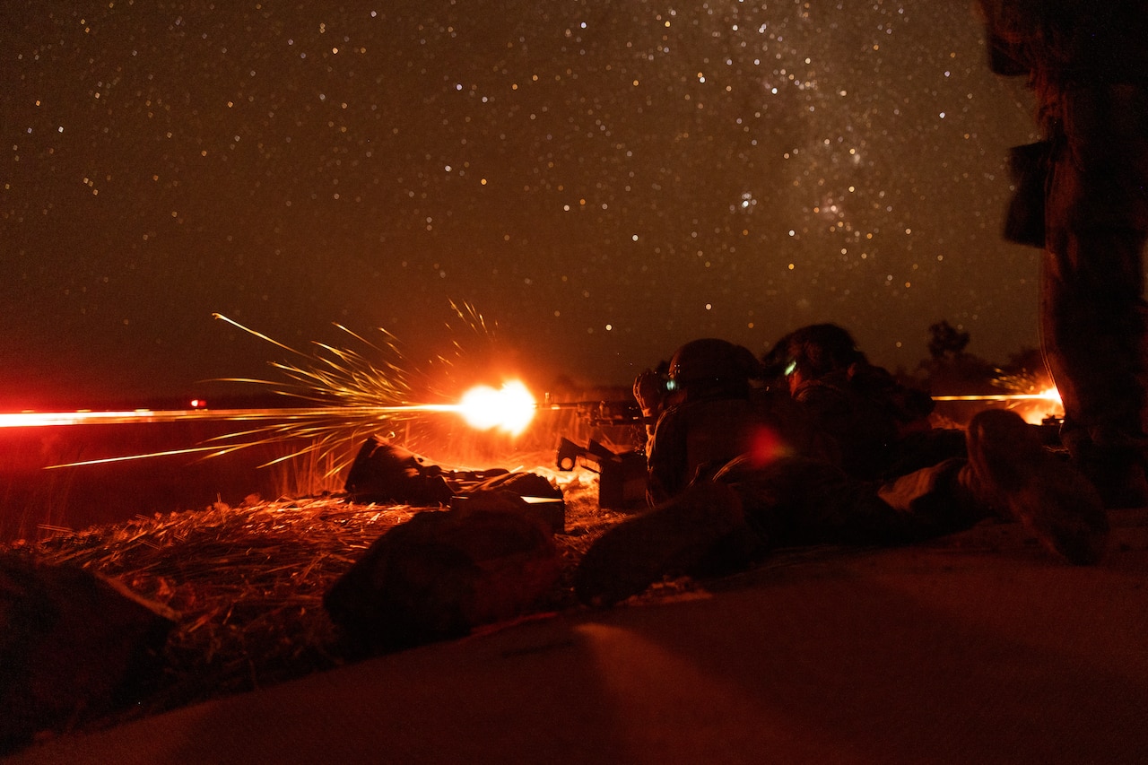 Marines fire a machine gun at night.