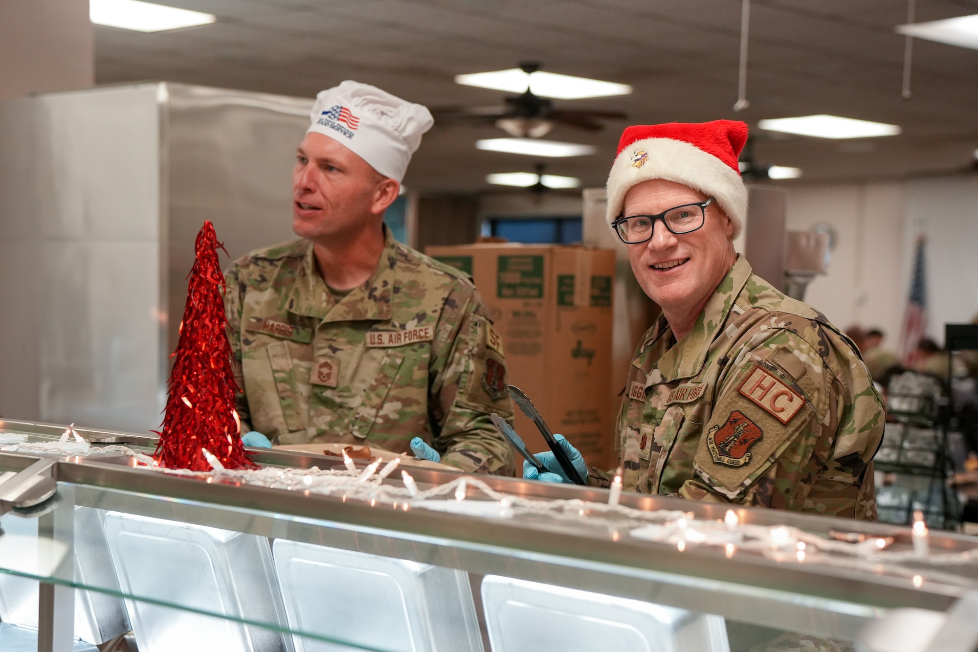 U.S. Air National Guard Chief Master Sgt. Chad Harris, left, security forces superintendent, and Maj. Joel Higgins, right, wing chaplain, 114th Fighter Wing, South Dakota National Guard, serve a holiday meal to Airmen during December's unit training assembly at Joe Foss Field, South Dakota, December 3, 2023.