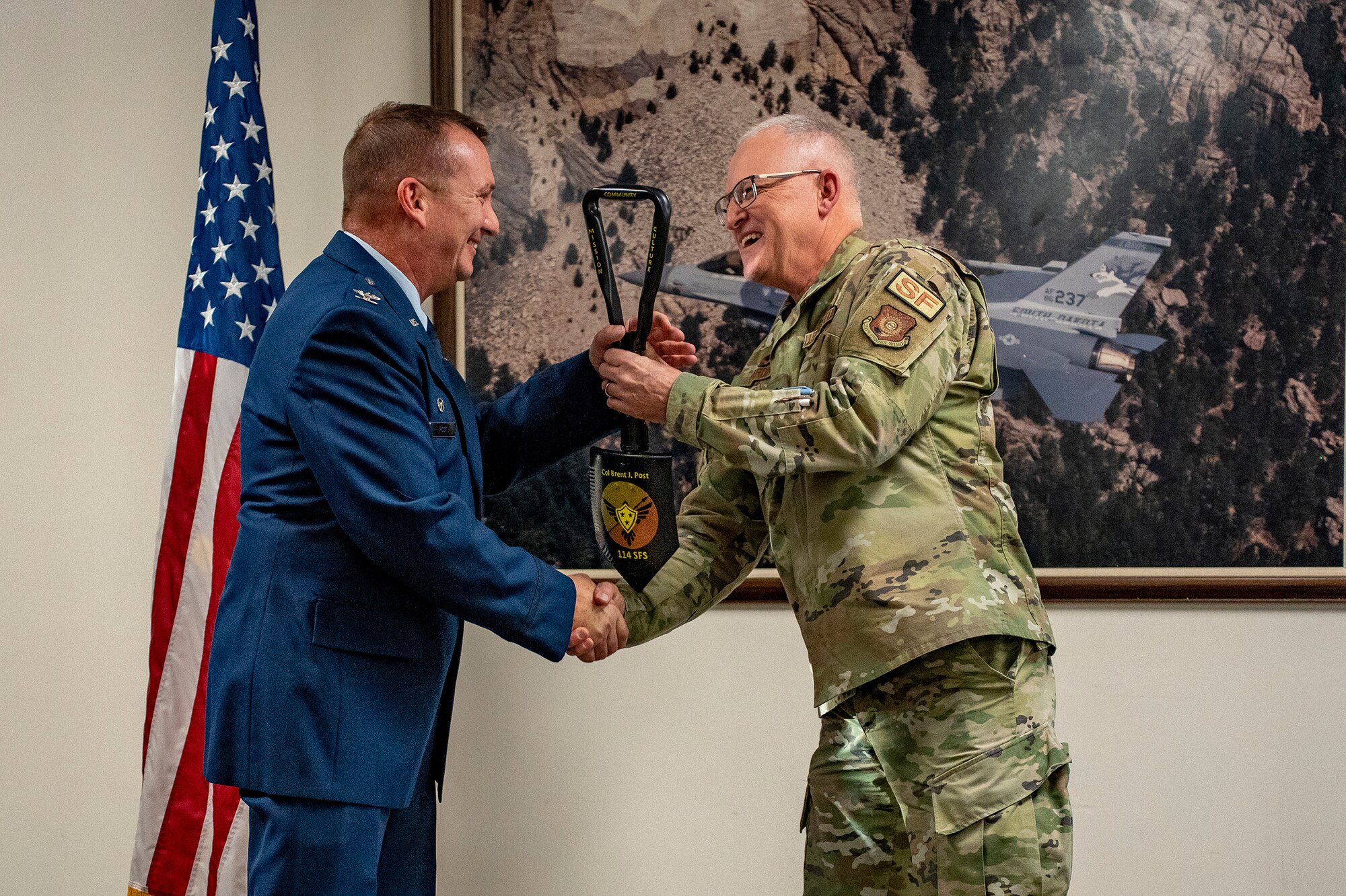 U.S. Air Force Lt. Col. Joseph Hardin, right, 114th Security Forces Squadron commander, presents U.S. Air Force Col. Brent Post, retired, with a commemorative entrenching tool at Post’s retirement ceremony at Joe Foss Field, S.D., Dec. 3, 2023.