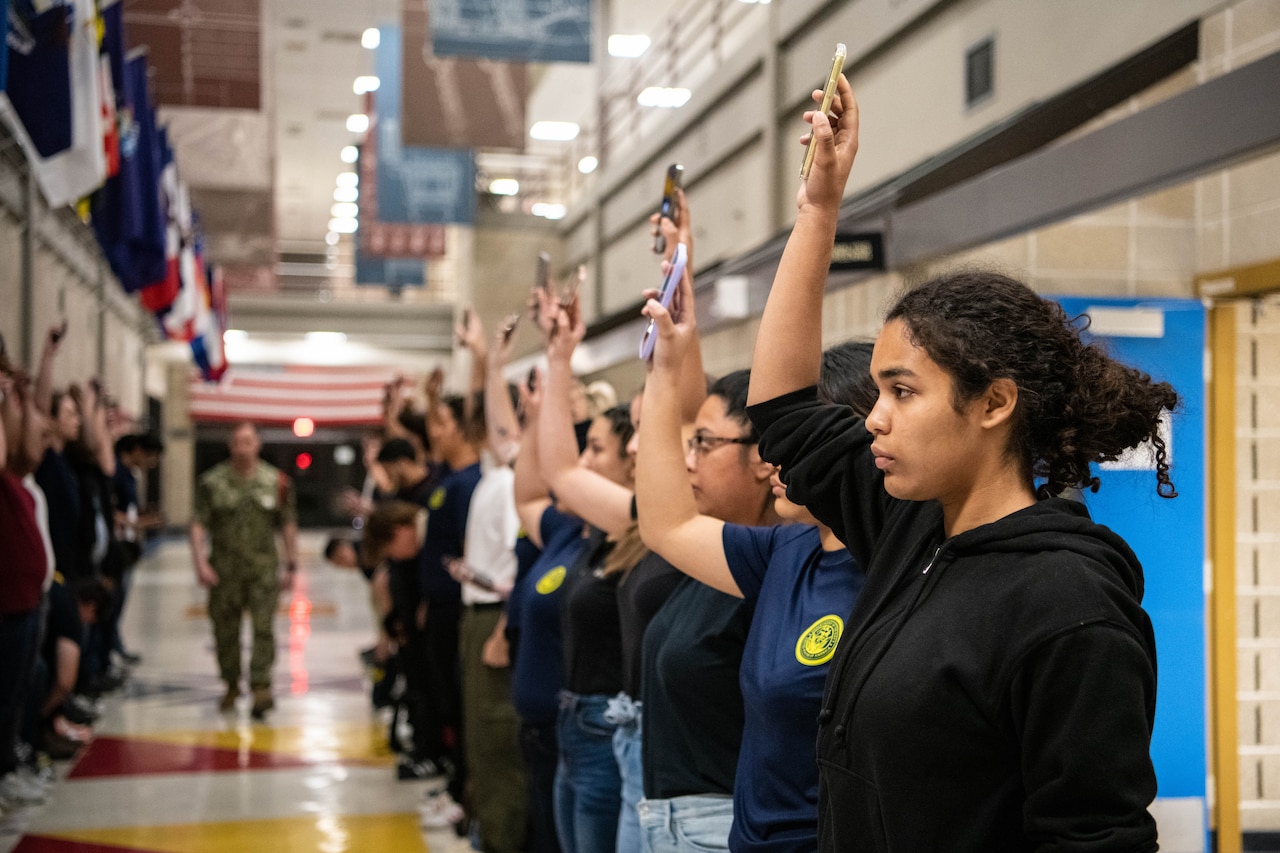 A service member is flanked by two rows of young civilians.