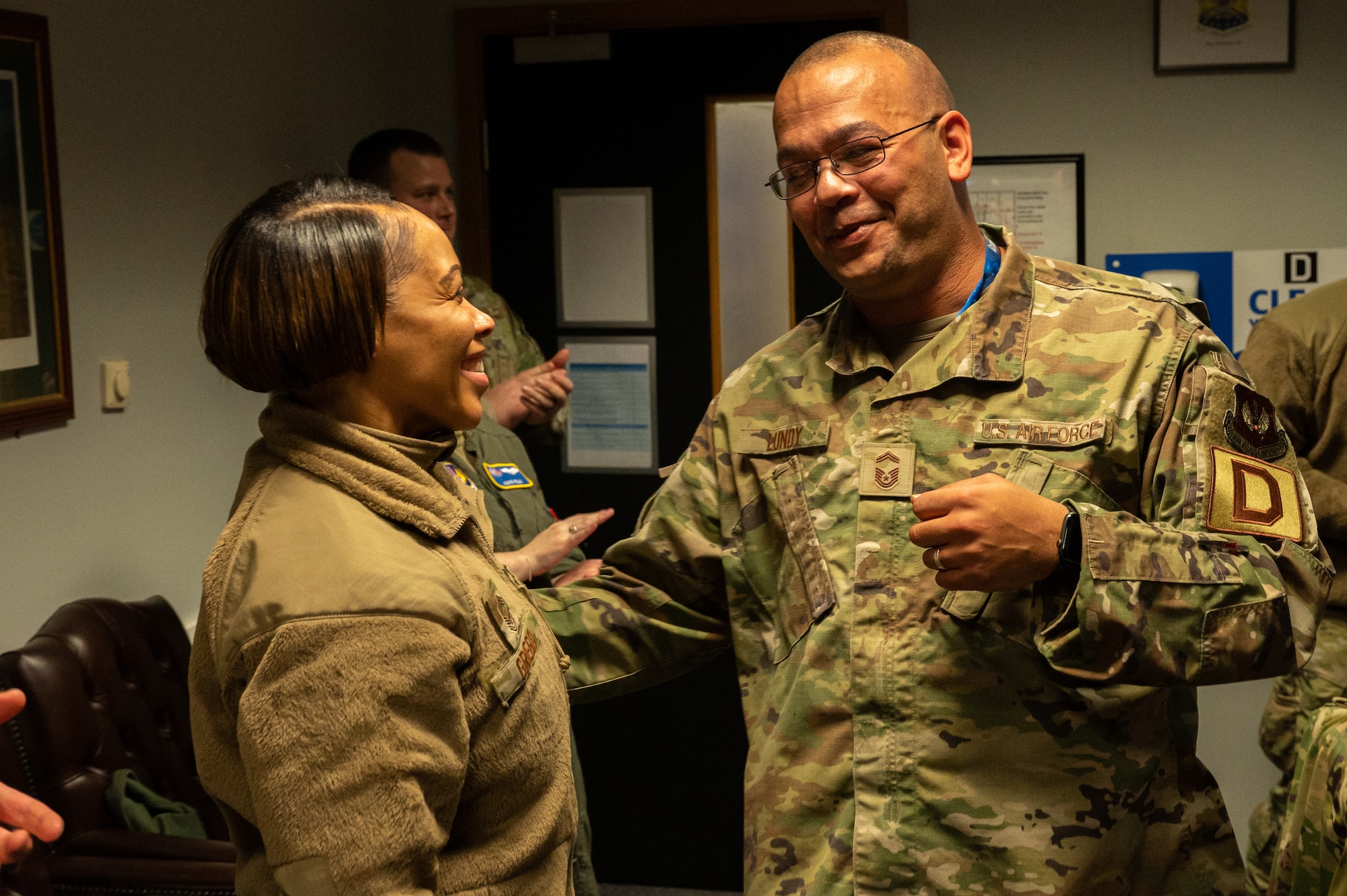 U.S. Air Force Chief Master Sgt. Tiffany Griego, left, 100th Air Refueling Wing command chief congratulates Senior Master Sgt. Jerome Lundy, right, 100th Maintenance Group quality assurance superintendent, after being notified that he will promote to the rank of chief master sergeant at Royal Air Force Mildenhall, England, Nov. 29, 2023.