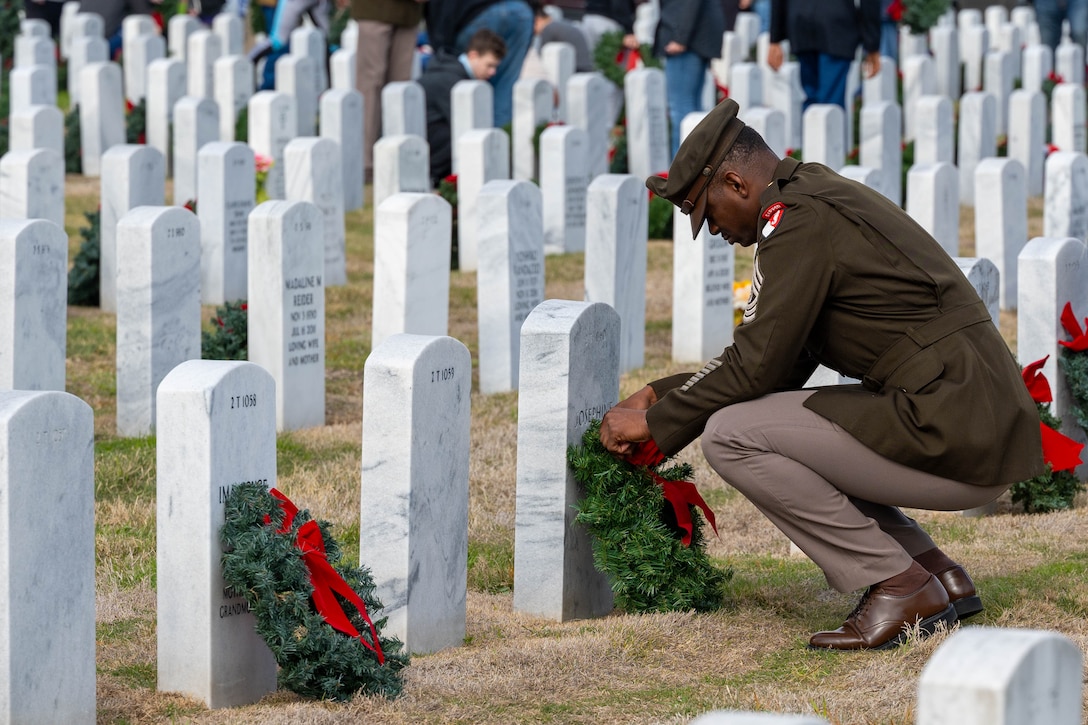 An Army officer places a wreath against the front of a headstone.