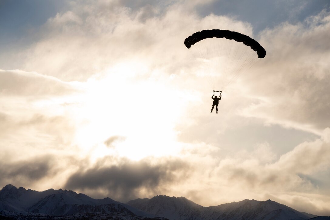 A paratrooper descends through a sunlit sky.