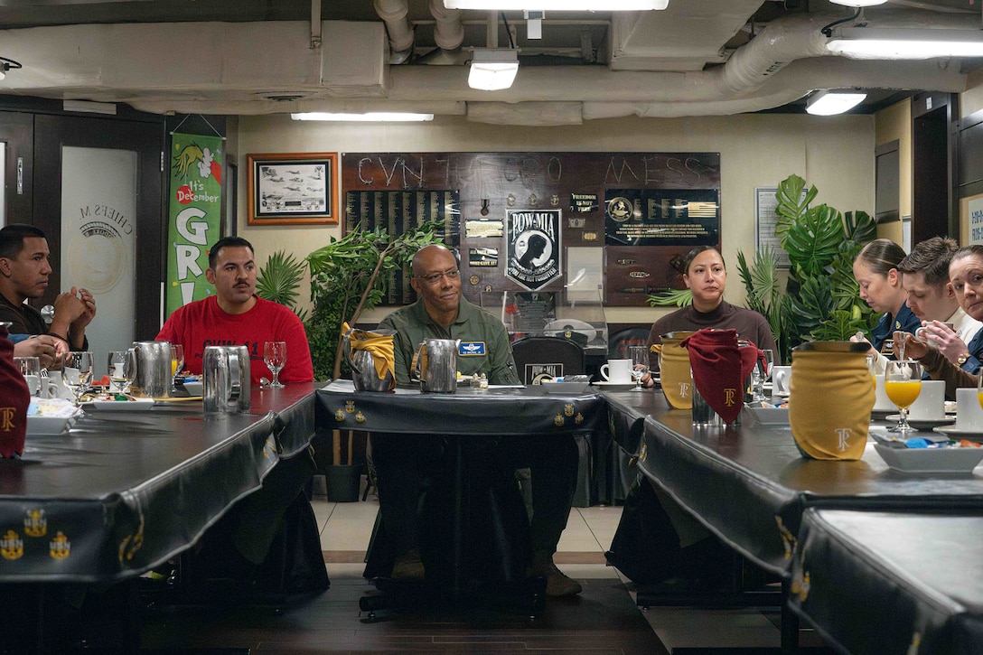 A group of people sit around a U-shaped table and eat.