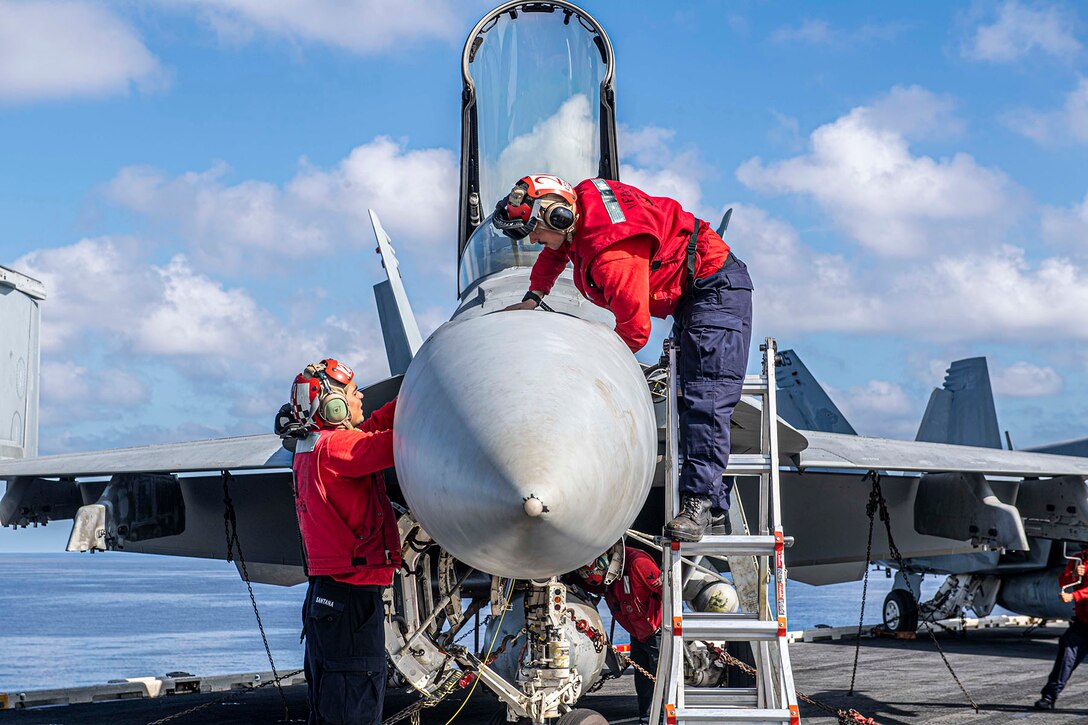 Two sailor install parts on an F/A-18E Super Hornet fighter jet.