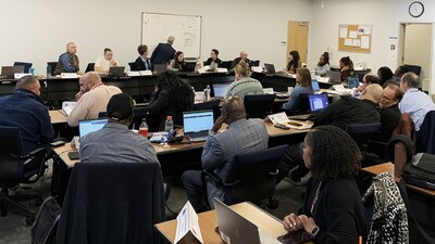 About 20 people sit at desks in a classroom