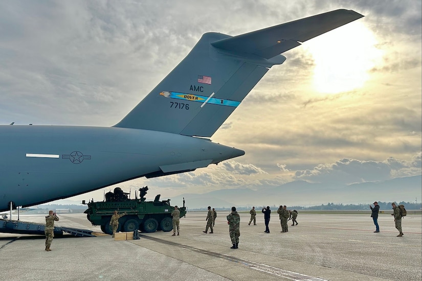 Soldiers stand on the tarmac near a military aircraft during daylight.