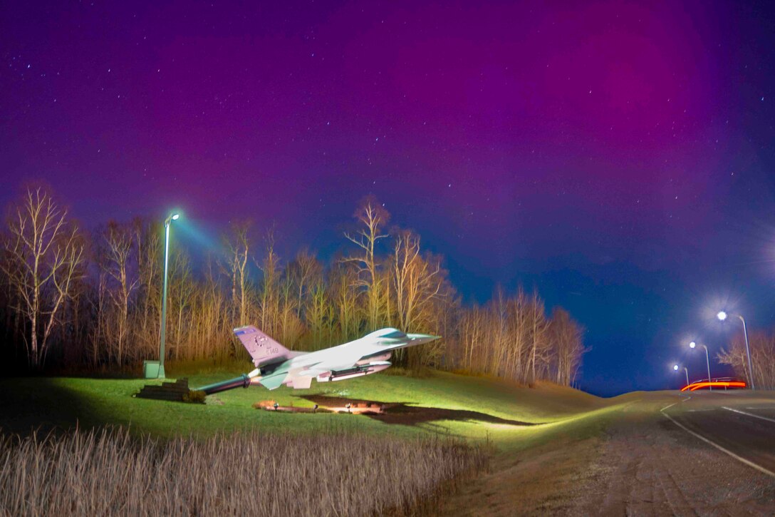 Purple/pink lights shine in the night sky over a static display of an aircraft.