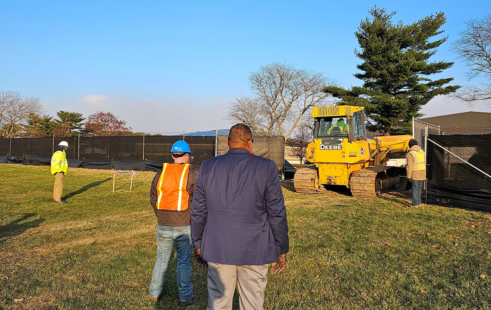 over the shoulder of people watching a bulldozer move dirt