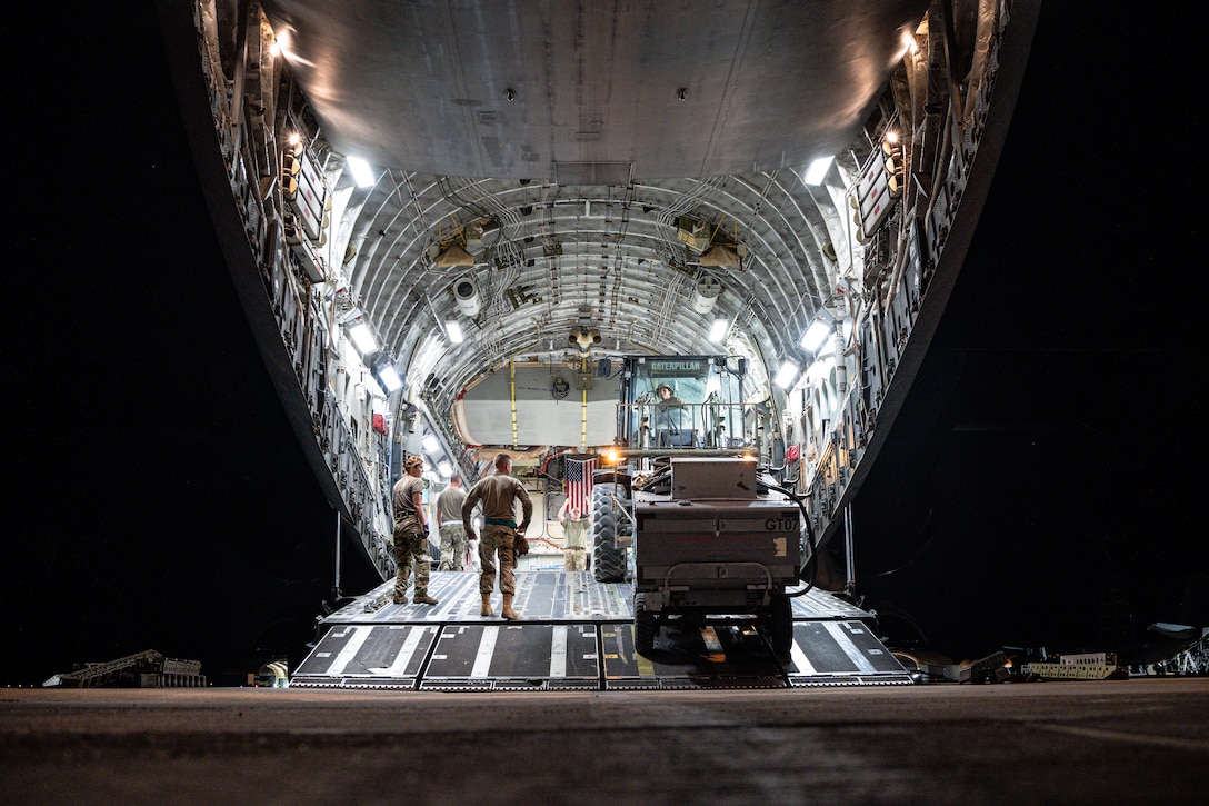 Airmen load cargo onto a large aircraft at night.