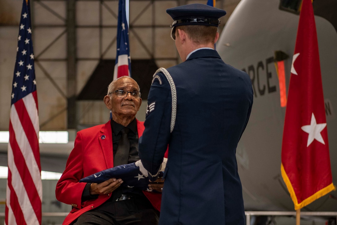 A service member in a formal uniform hands a folded American flag to a  Tuskegee Airman.