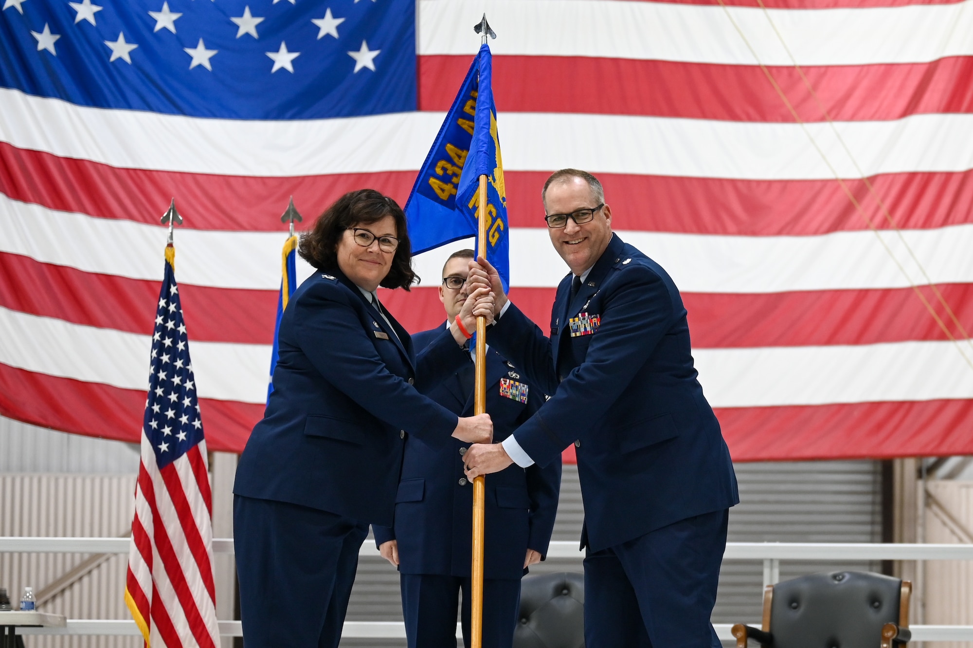 Lt. Col. David Borden, 434th Mission Support Group commander, accepts the guidon from Col. Summer Fields, 434th Air Refueling Wing commander, during a change of command ceremony. Both are standing on a stage, facing each other, with a large American flag behind them.