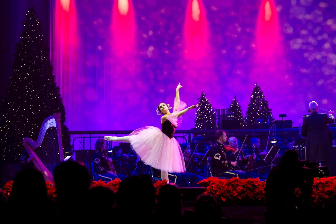 A ballet dancer performs on stage in front of an orchestra.