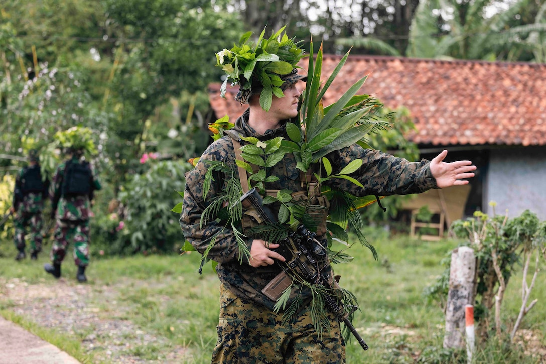 A Marine in camouflage uses his left hand to gesture in a direction.