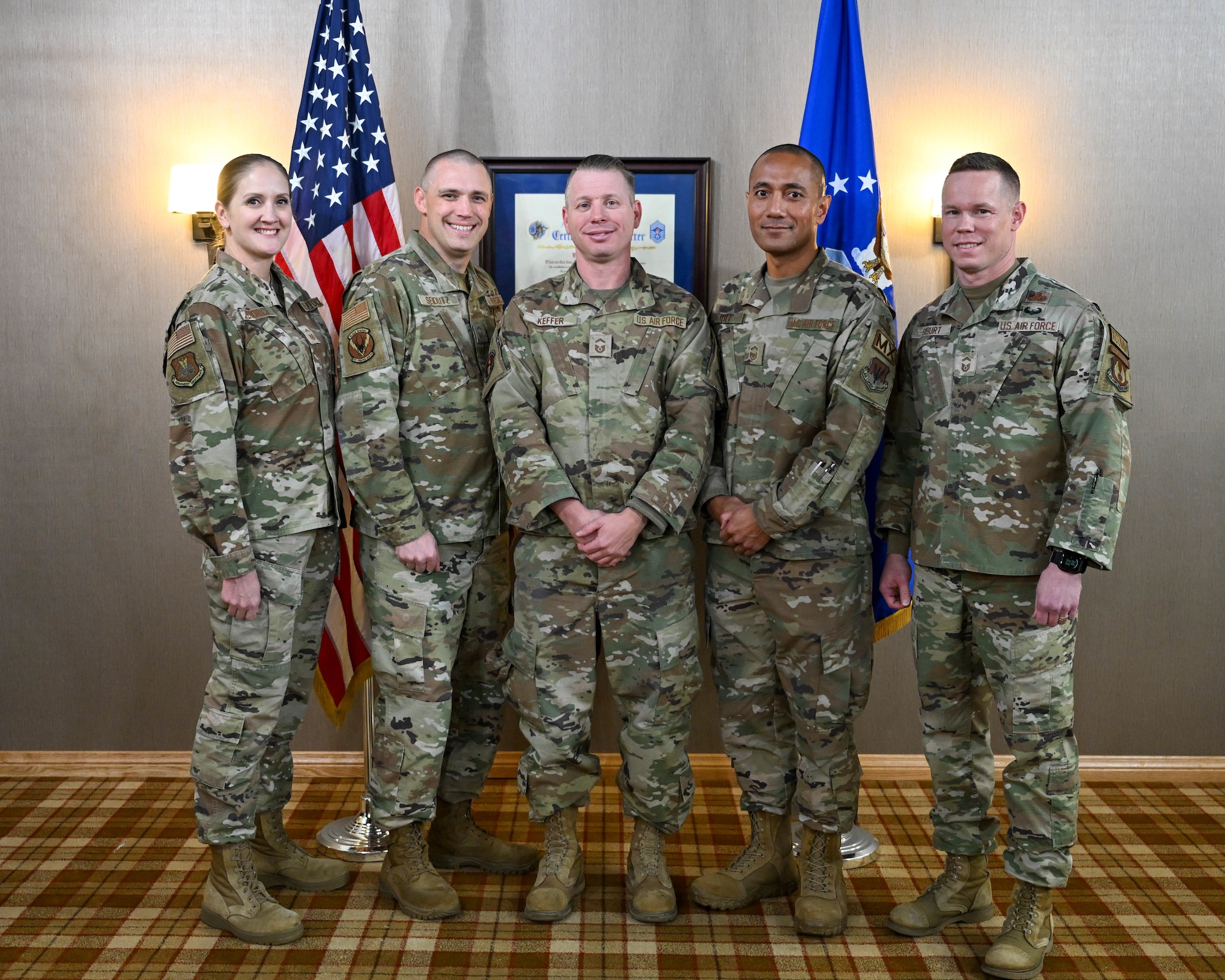 Five members in uniform stand in front of an American flag and an Air Force military flag