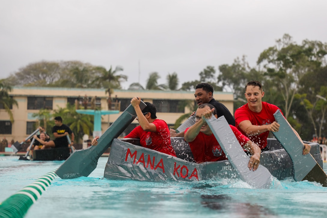 Soldiers paddle a boat made from cardboard boxes and duct tape in a pool.