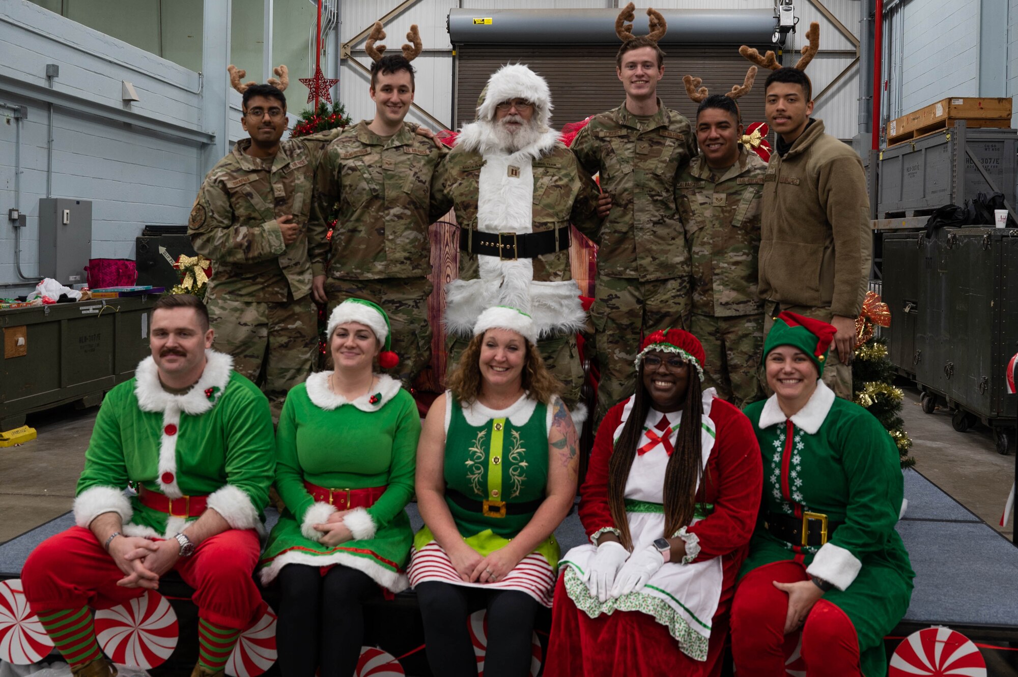 Uniformed Airmen and civilian employees in holiday attire pose with Santa during a group photo.