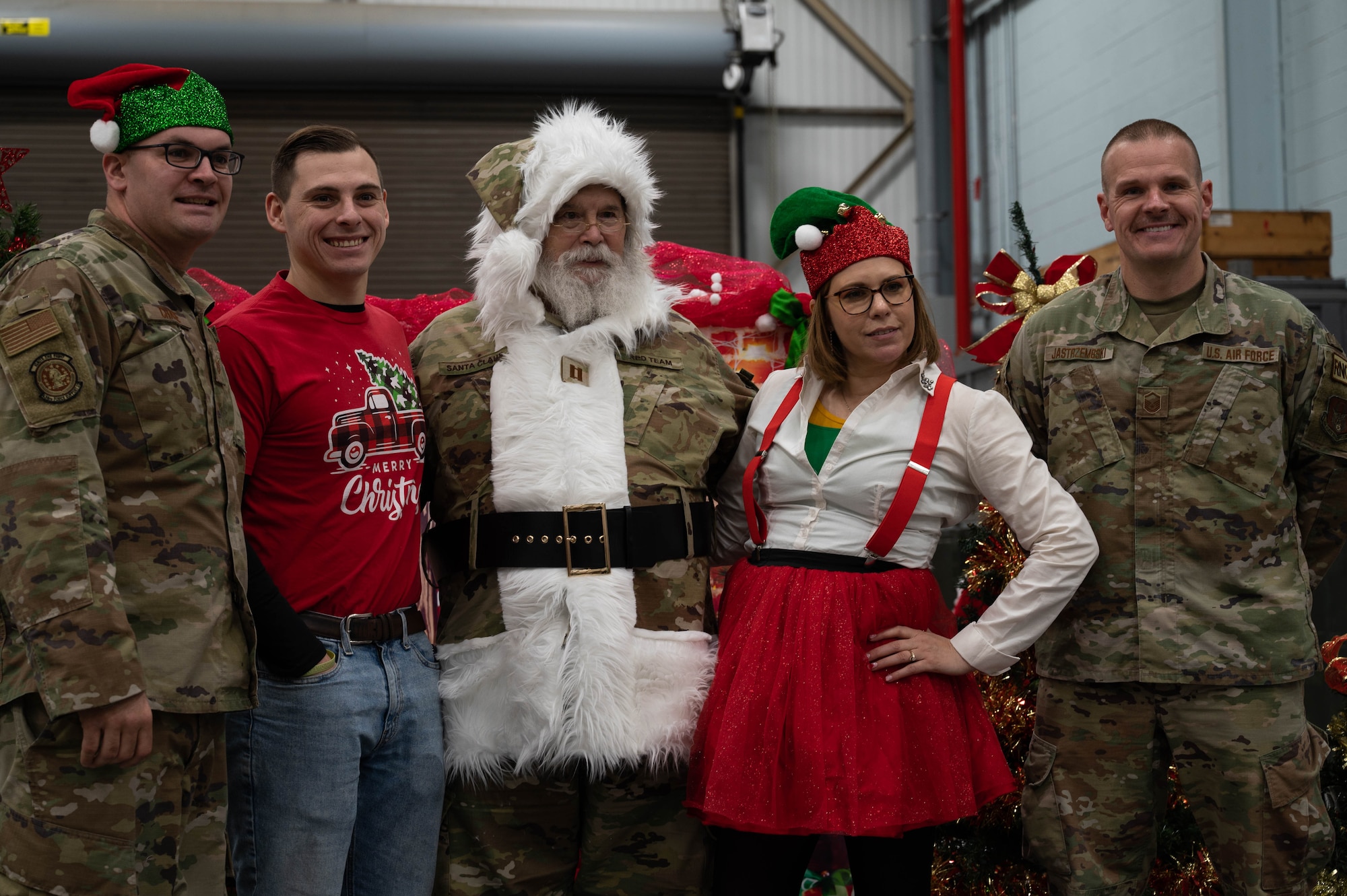 A small group of uniformed Airmen and civilian employees in holiday attire pose with Santa for a photo.