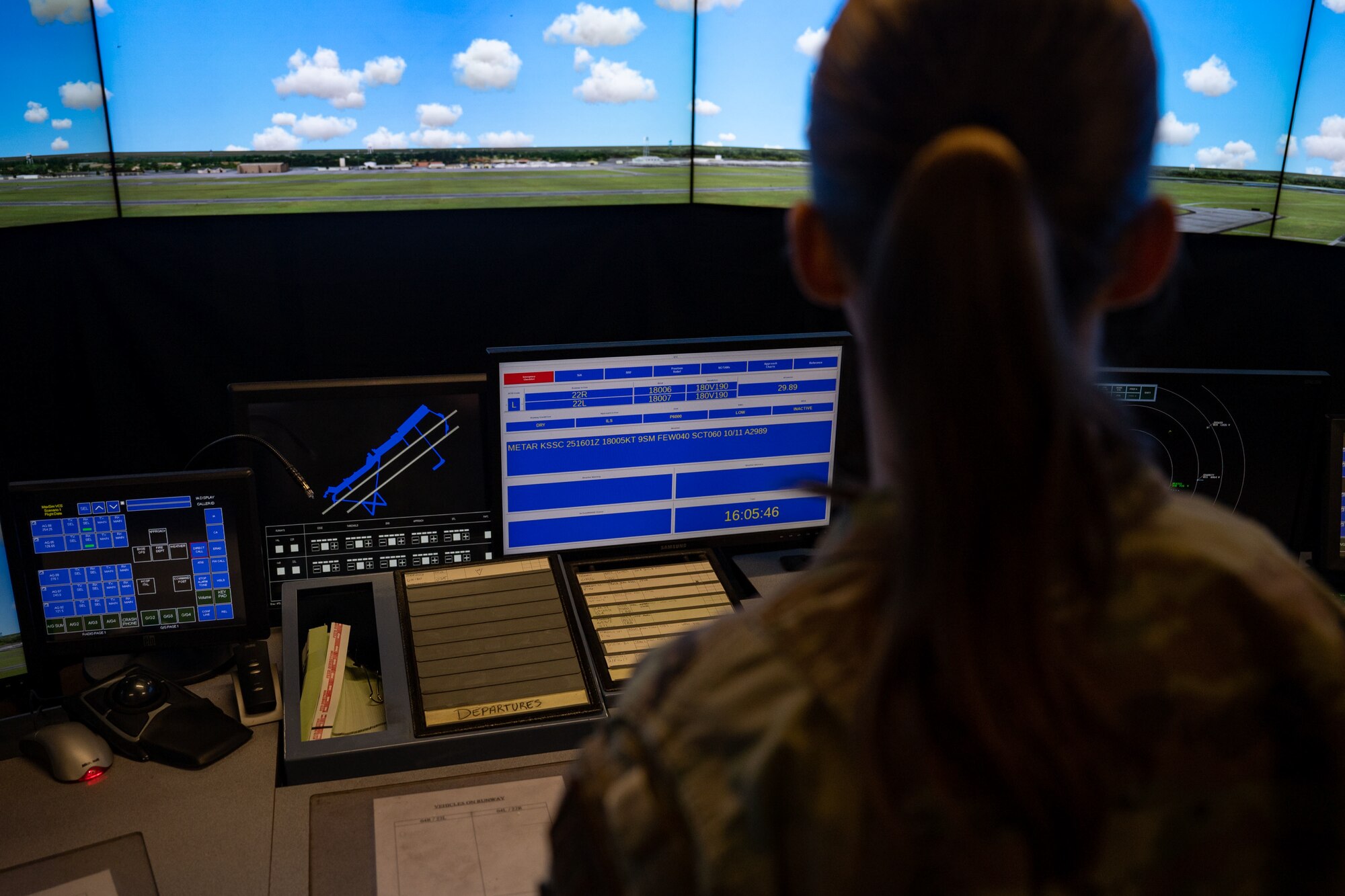 female airman stands in front of and looks at screes showing blue sky and flightline