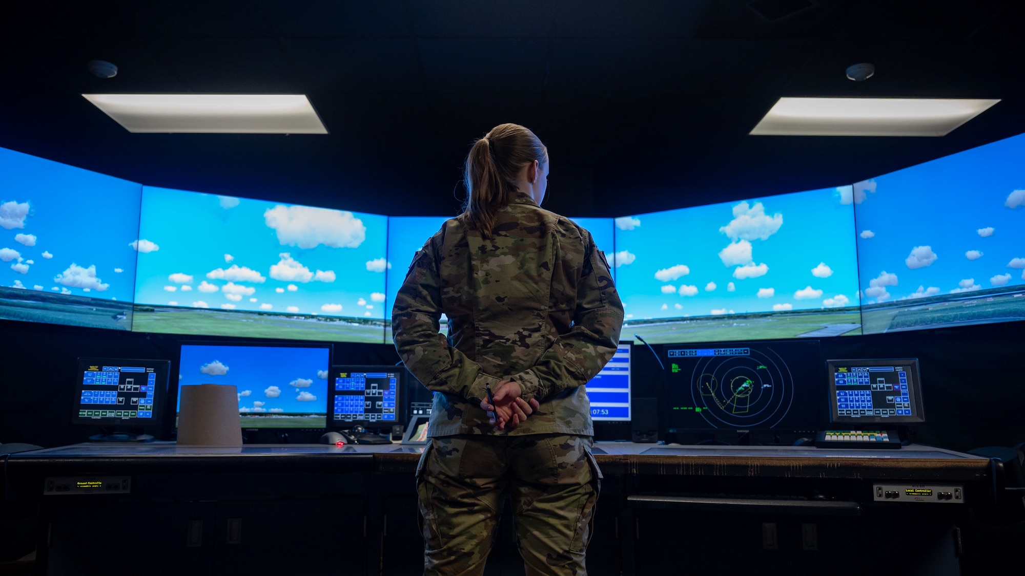Female airman stands with hands behind her back in front of screens showing blue sky