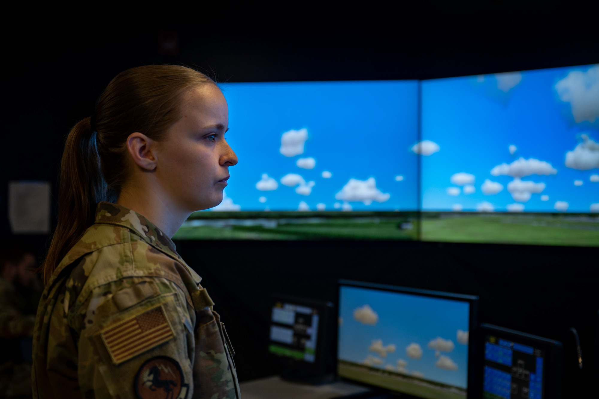 Female airman looks to the right in front of bright screen showing blue sky