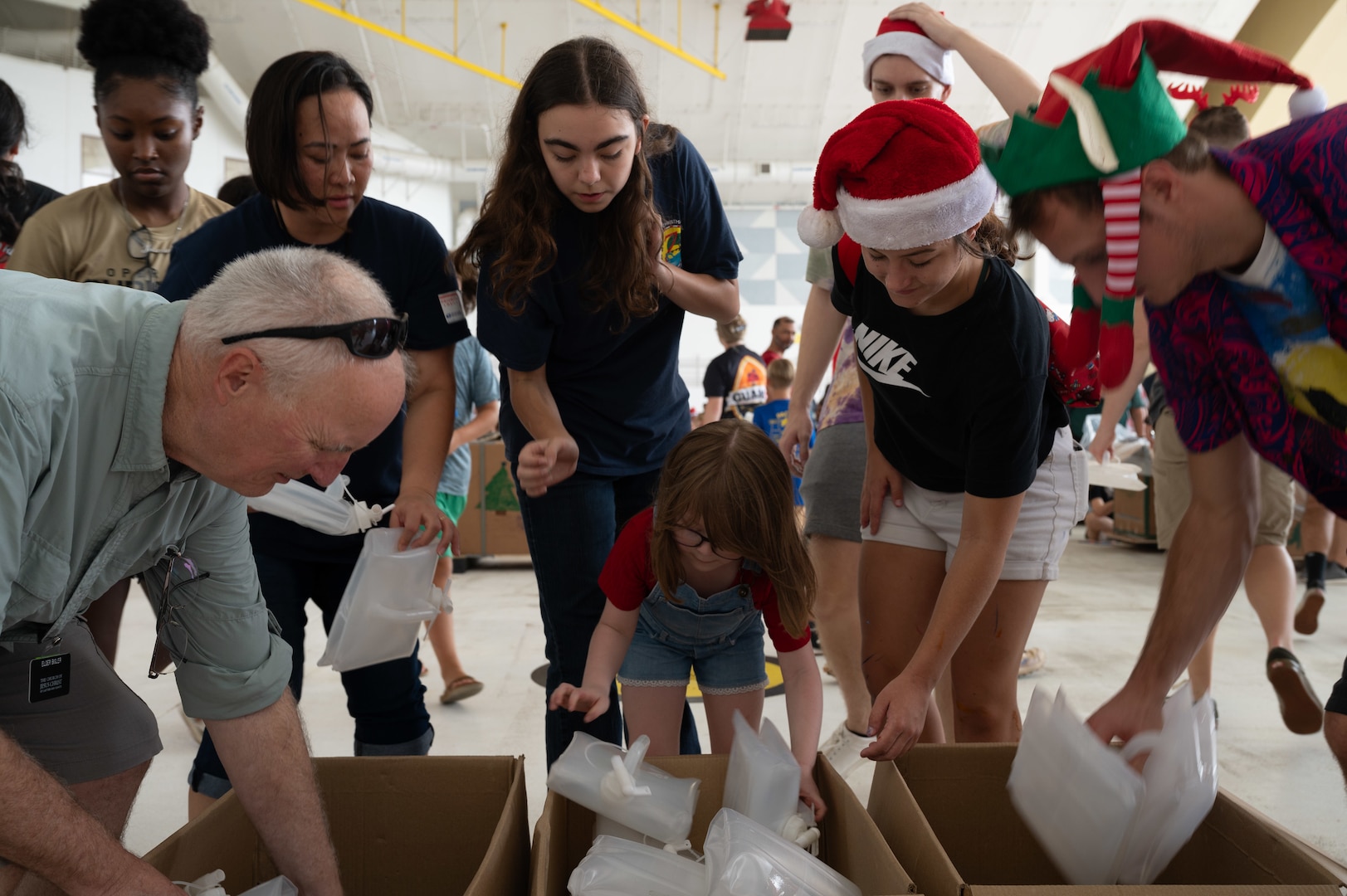 U.S. Air Force members assigned to the 36th Expeditionary Airlift Squadron and children collect items to fill a bundle of humanitarian aid during the annual bundle building event in support of Operation Christmas Drop 2023 (OCD 23) at Andersen Air Force Base, Guam, Dec. 2. 2023. The tradition began during the Christmas season in 1952 when a B-29 Superfortress aircrew saw islanders waving at them from the island of Kapingamarangi, 3,500 miles southwest of Hawaii. In the spirit of Christmas, the aircrew dropped a bundle of supplies attached to a parachute to the islanders below, giving the operation its name. Today, airdrop operations include more than 50 islands throughout the Pacific. (U.S. Air Force photo by Senior Airman Brooklyn Golightly)