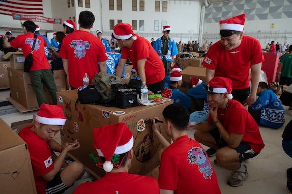 Members of the Republic of Korea Air Force (ROKAF) gather to decorate a bundle box during the annual bundle building event in support of Operation Christmas Drop 2023 (OCD 23) at Andersen Air Force Base, Guam, Dec. 2, 2023. OCD is the Department of Defense’s longest-running humanitarian airlift operation. The tradition began during the Christmas season in 1952 when a B-29 Superfortress aircrew saw islanders waving at them from the island of Kapingamarangi, 3,500 miles southwest of Hawaii. In the spirit of Christmas, the aircrew dropped a bundle of supplies attached to a parachute to the islanders below, giving the operation its name. Today, airdrop operations include more than 50 islands throughout the Pacific. (U.S. Air Force photo by Senior Airman Brooklyn Golightly)