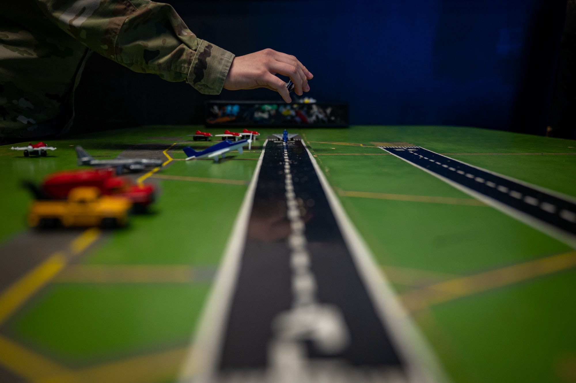 hand places small model airplane on a green board with a black runway