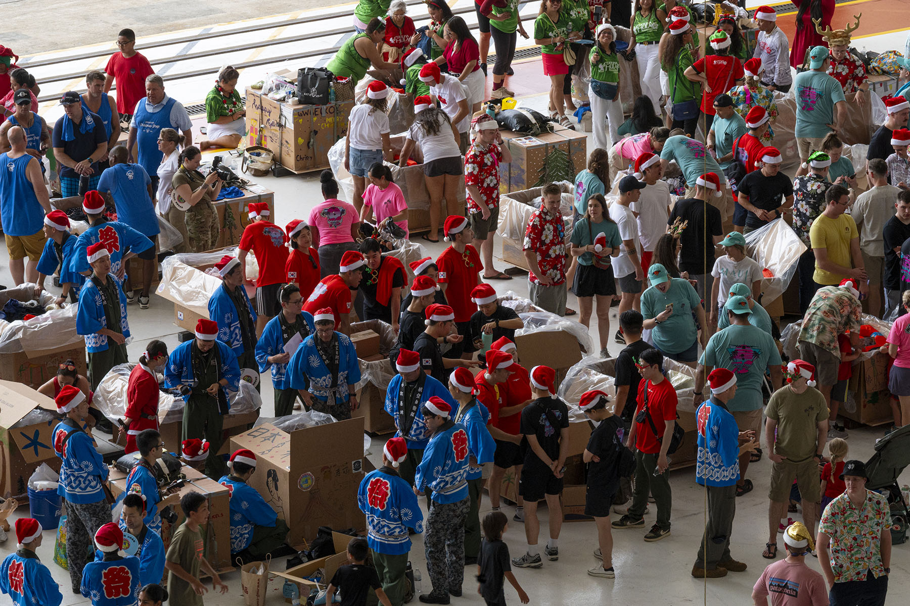 A large group of people in festive garb decorate large cardboard boxes, seen from above. 