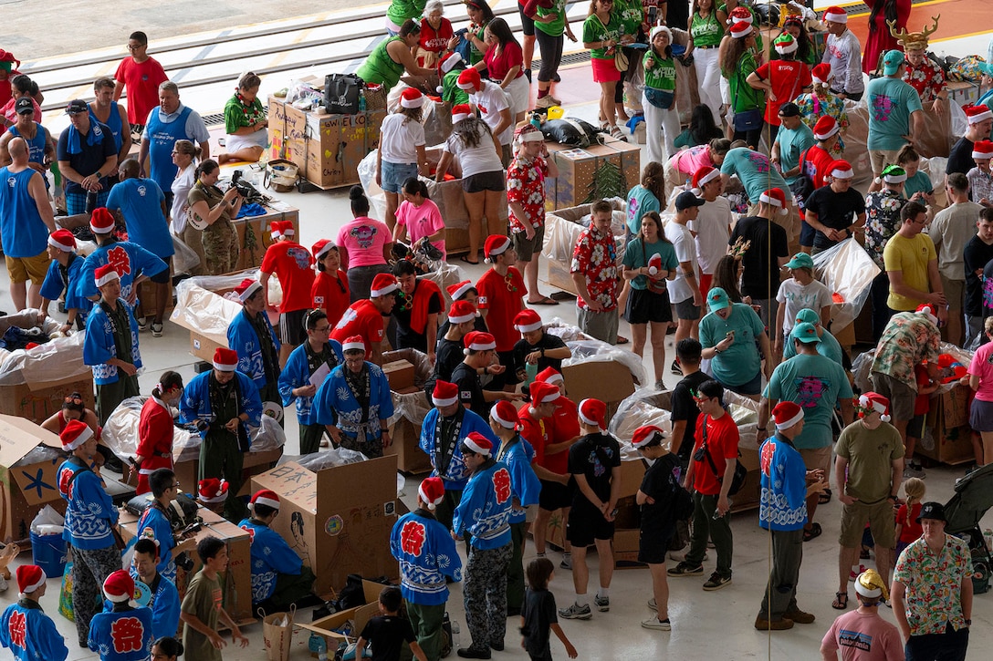 Overhead view of dozens of people in holiday garb decorating cardboard boxes in a large room.